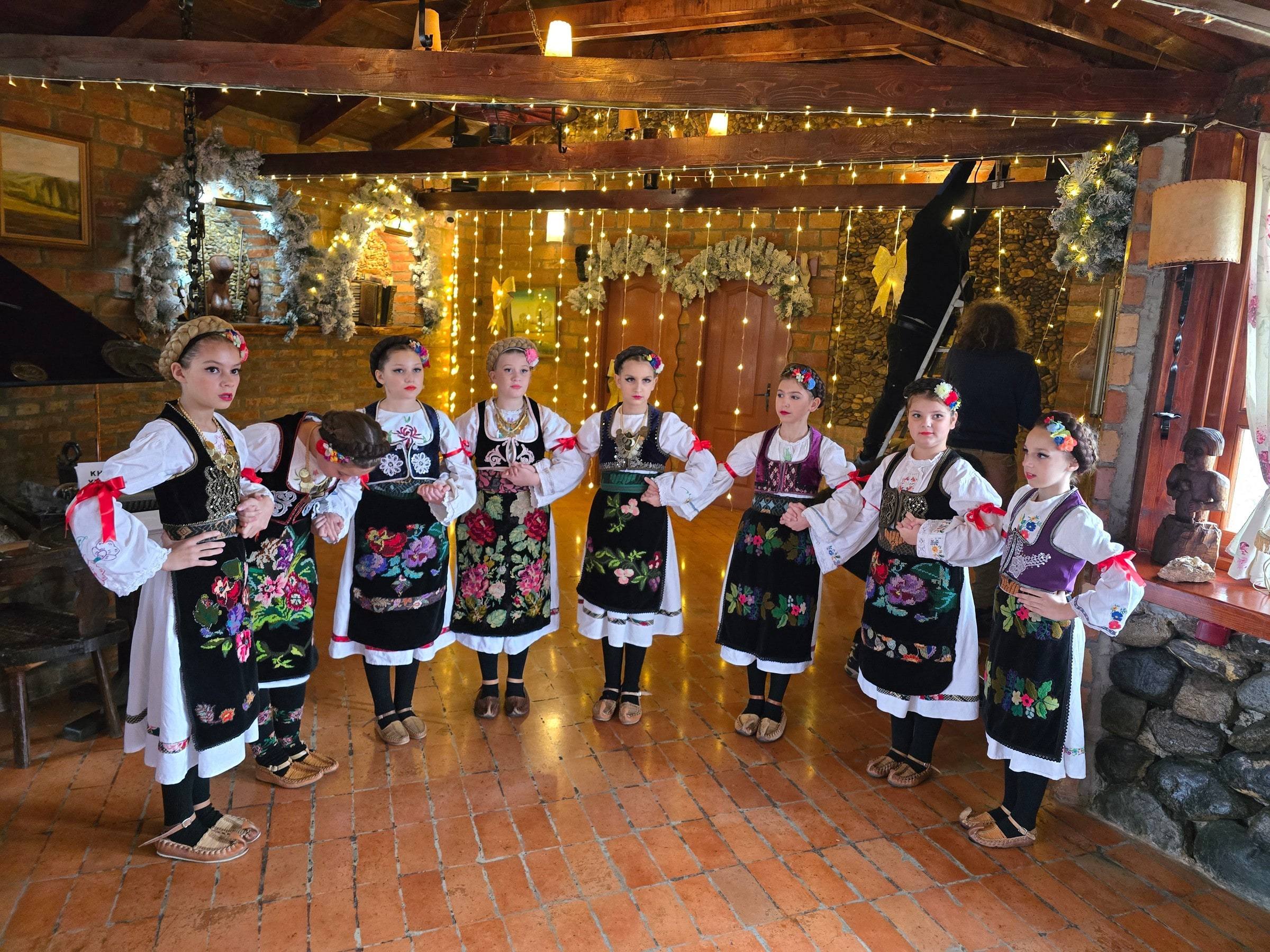 Dečji folklorni ansambl u nošnjama, u restoranu ukrašenom za Novu godinu