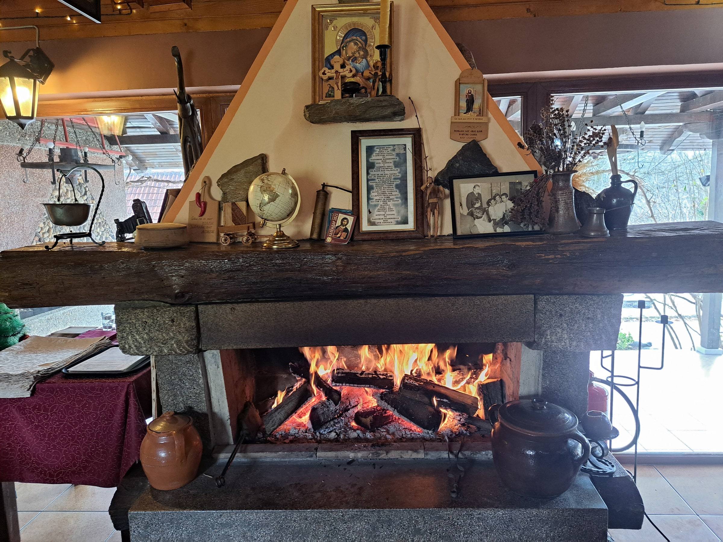 Kameni kamin sa vatrom u restoranu Dobrosav, iznad njega ikona i stari predmeti