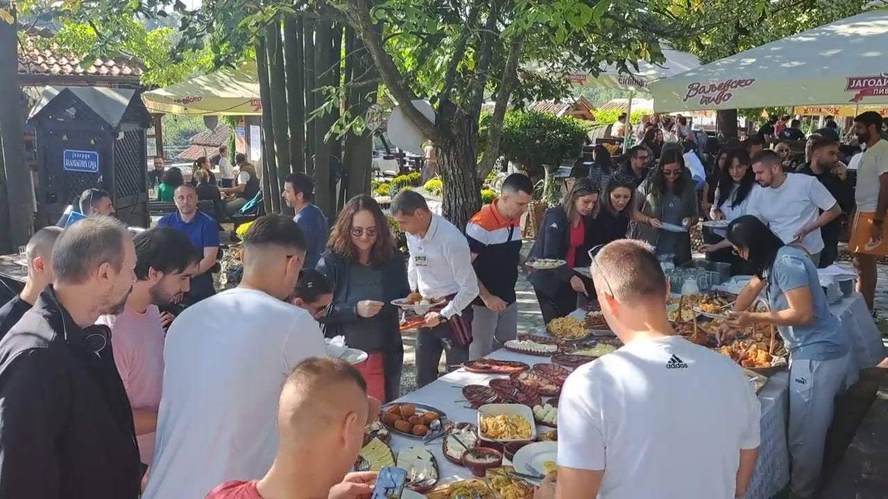 Veliko društvo za švedskim stolom u bašti, pored natpisa „Trpeza radosti“