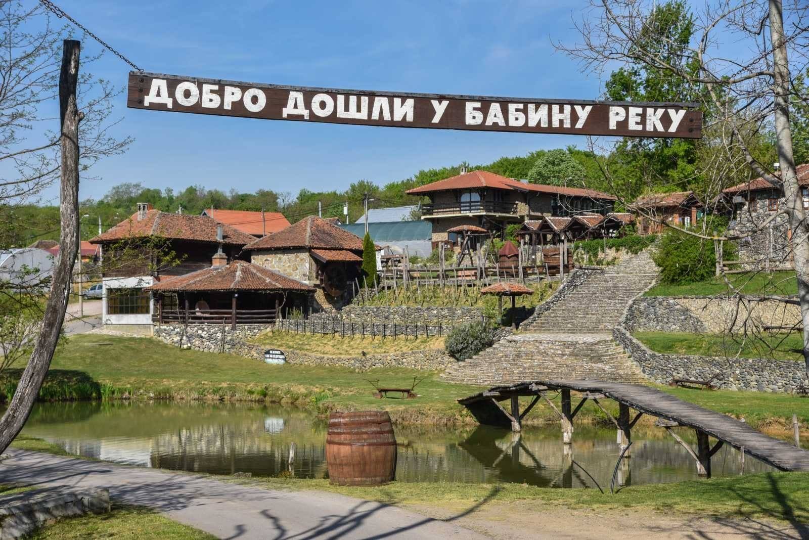 Drveni most preko jezera, natpis „Dobro došli u Babinu reku“ i restorani na brdu