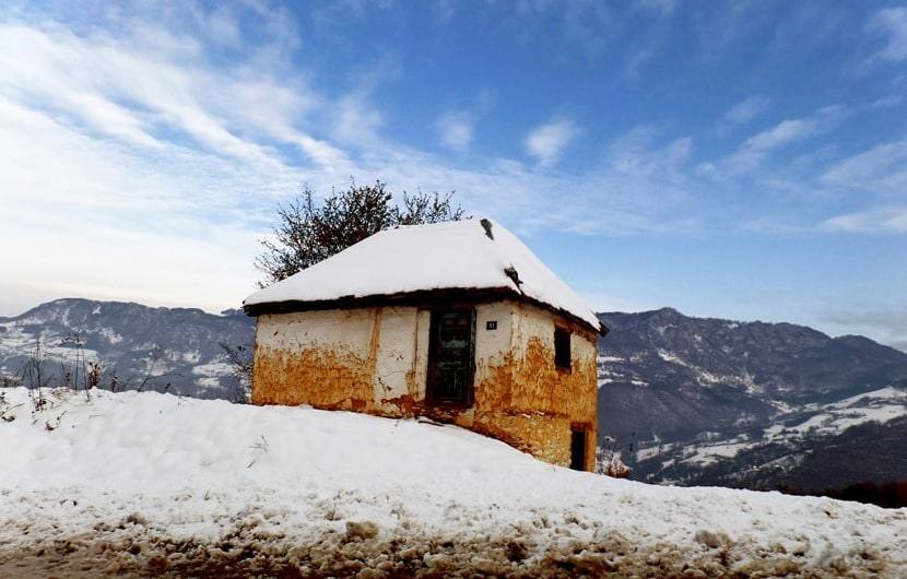 Stara kuća pod snegom, na brdu iznad doline