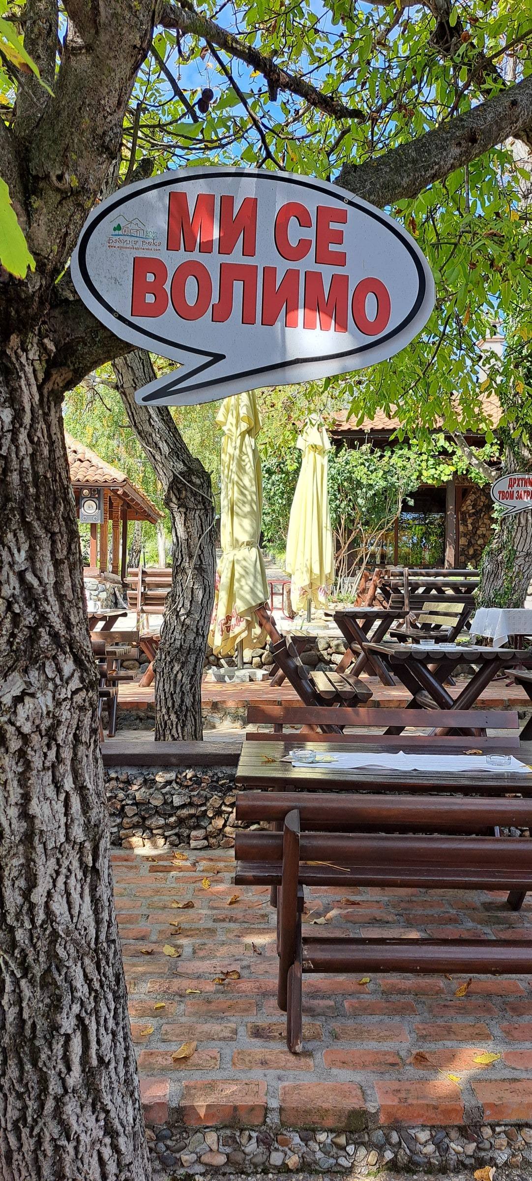 Tabla u obliku oblačića „Mi se volimo“ na drvetu iznad stolova u bašti