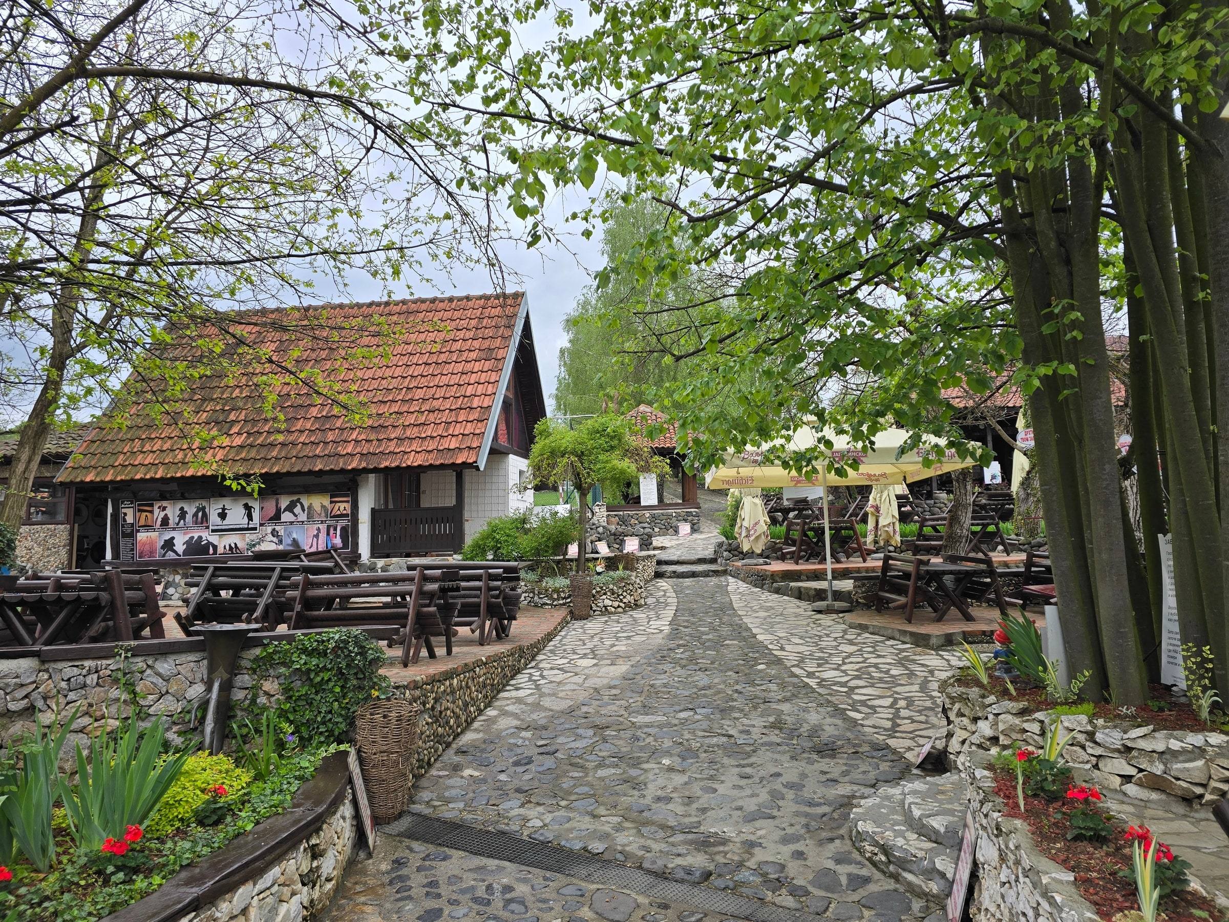 Kaldrmisana staza kroz dvorište u proleće, sa crvenim cvećem i drvenim stolovima
