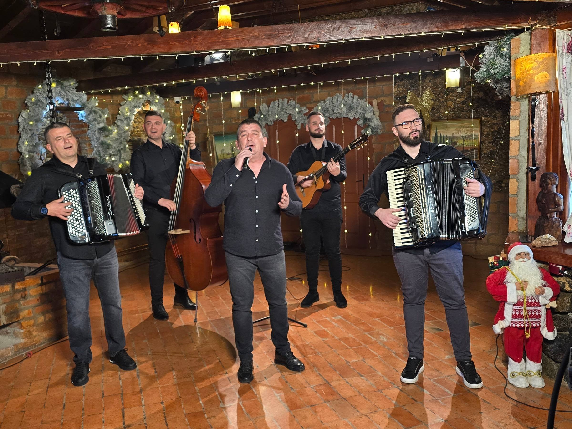 Muzičari sa harmonikama i kontrabasom sviraju u restoranu, pored jelke